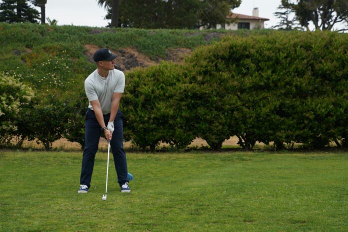 Photo by Ryan Hoffman a man holding a golf club on top of a green field