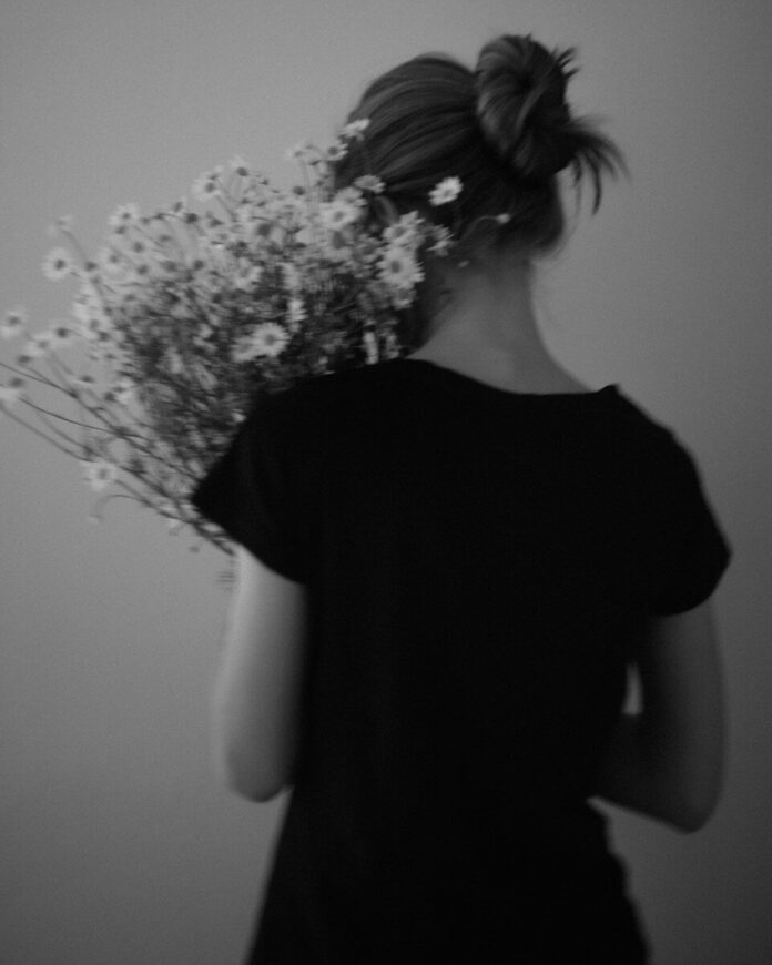 Photo by Alina Chernovolova A person in a black shirt holding a bouquet of daisies